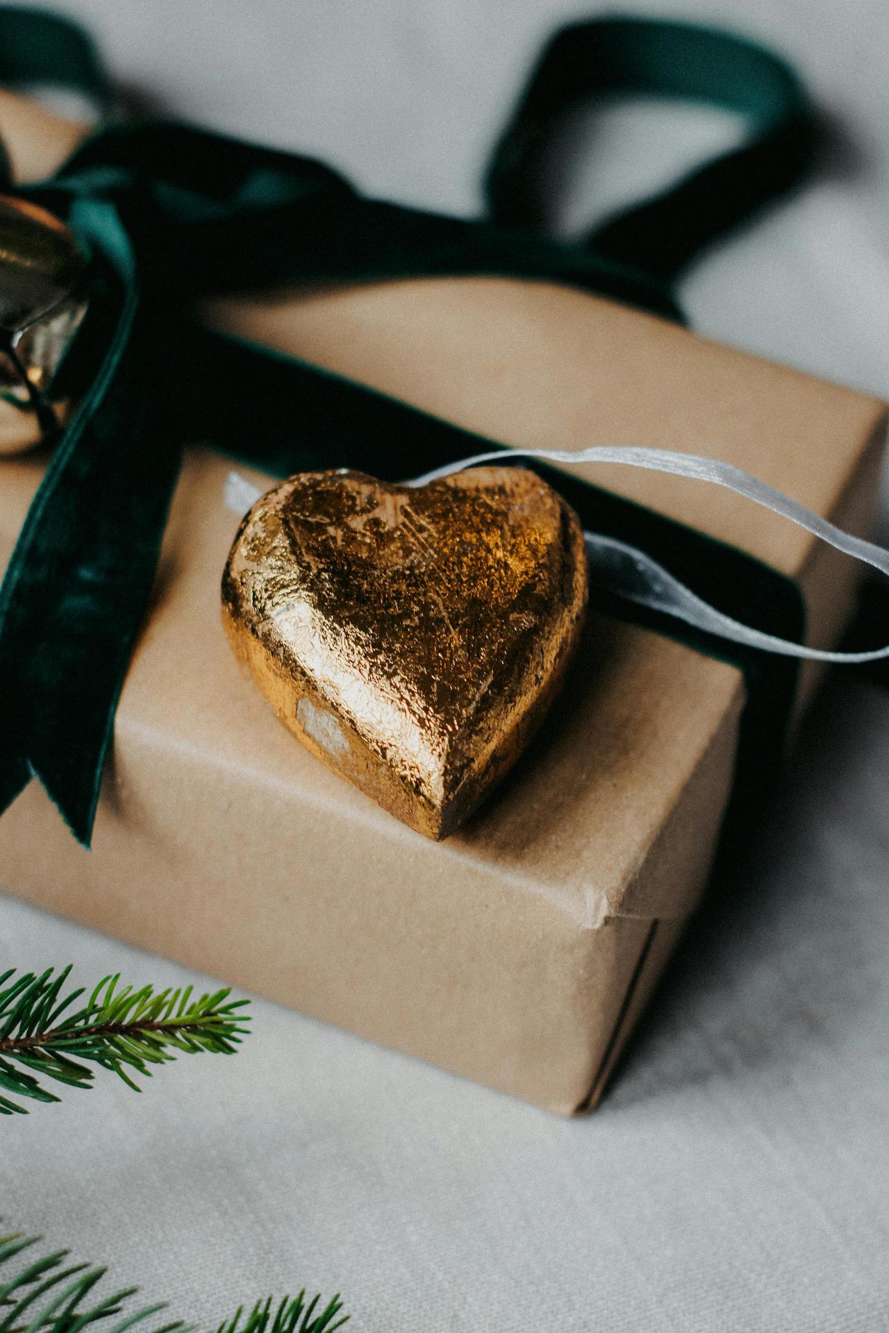 Close-up of a wrapped gift box adorned with a golden heart ornament and green ribbon.